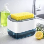 موزع الصابون مودرن باللون الأبيض والرمادي على حوض المطبخ بجانب ليمونة وعبوة منظف.