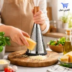 المبشرة اليدوية الاستانلس بتصميم هرمي انيق بجانب قطع الجبن الشيدر والرومي على خلفية زرقاء استوديو
