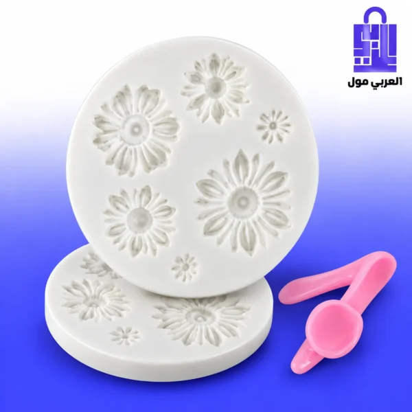 قالب سيليكون أبيض دائري متعدد التجاويف لأشكال زهور الأقحوان (Daisy) بأحجام مختلفة على خلفية رخامية مع تورتة مزينة وملاعق وردية